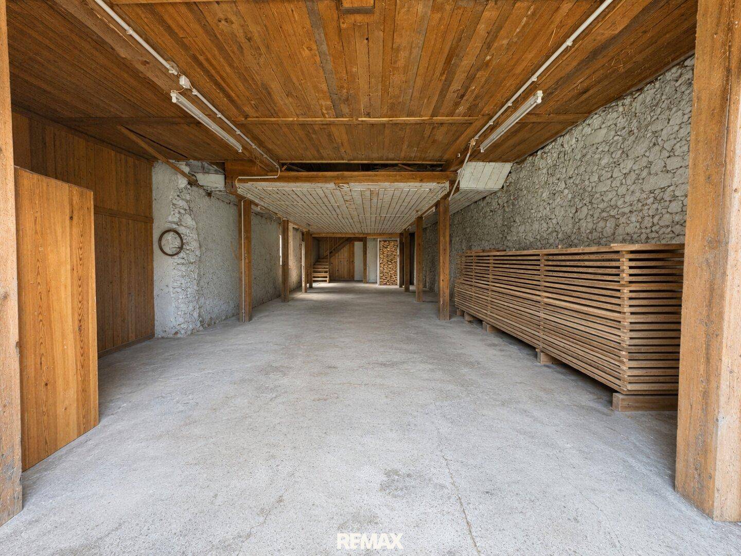 Großer Lagerraum mit Holzbalken, Steinwänden und gestapeltem Holz, ideal für Vorräte.