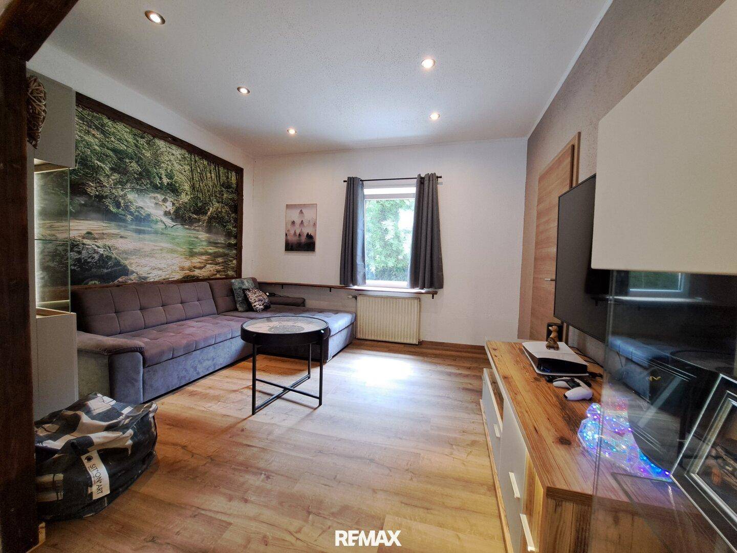 Wohnzimmer mit großem Ecksofa, Fernseher und einem Fenster, das viel Licht hereinlässt.