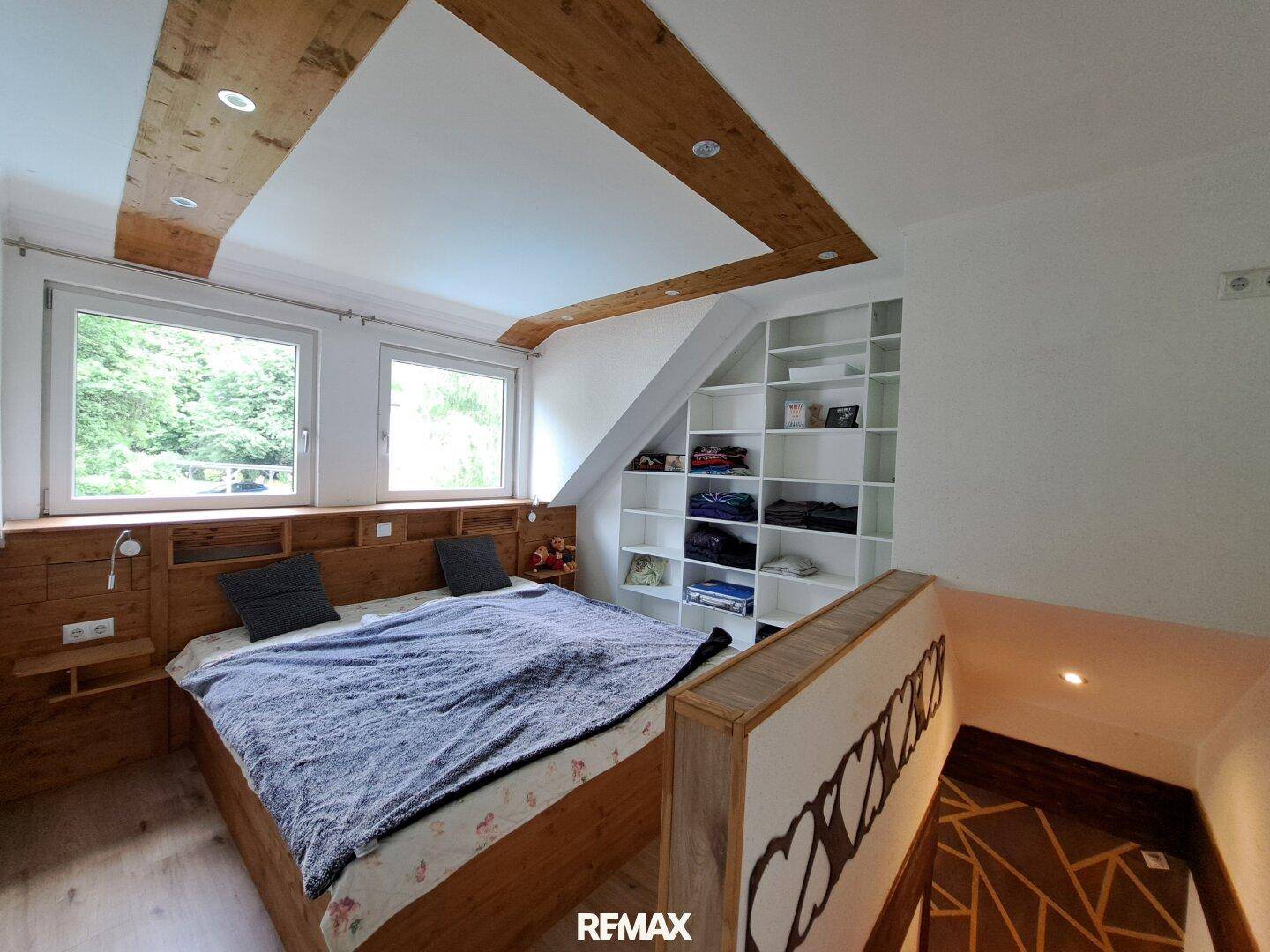 Gemütliches Schlafzimmer mit Holzbett, Einbauregalen und Dachschrägen, hell durch große Fenster.