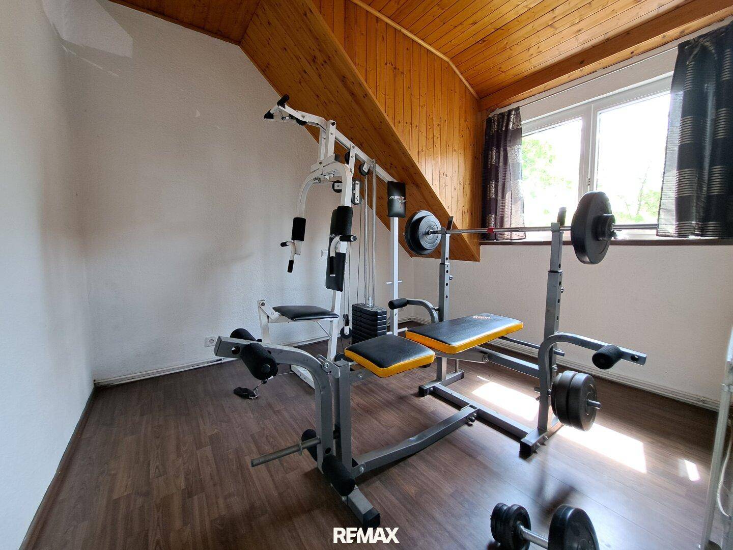 Fitnessraum im Dachgeschoss mit Trainingsgeräten, Holzbalken und Laminatboden.