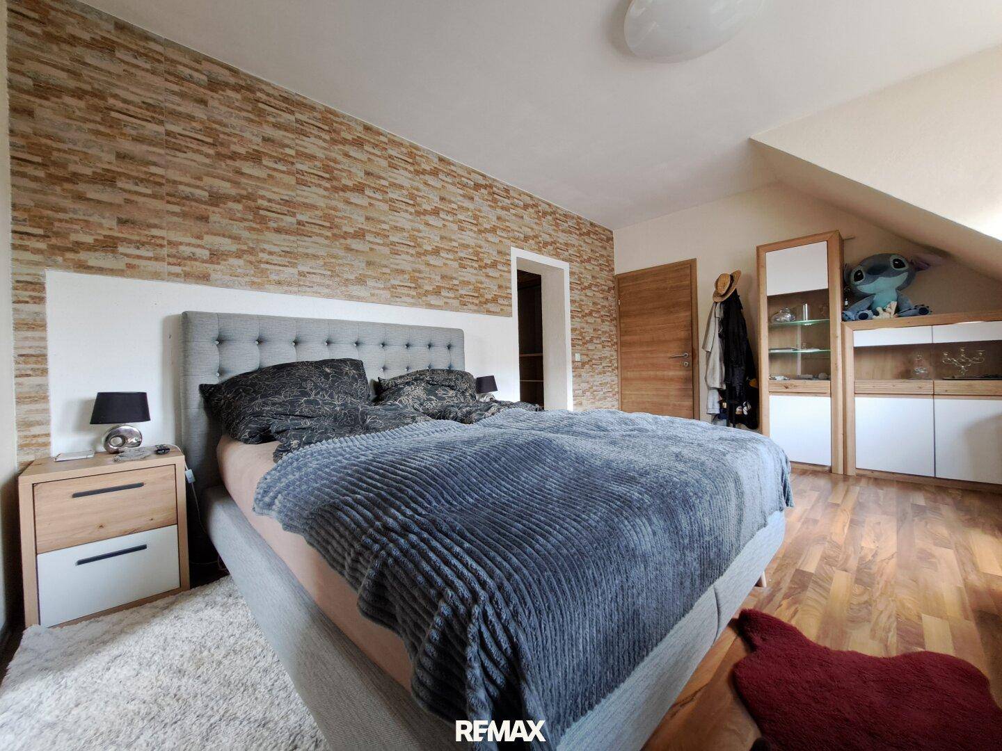 Gemütliches Schlafzimmer mit Doppelbett, dekorativer Steinwand und Holzmöbeln.