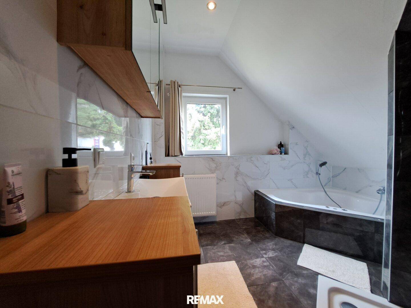 Modernes Badezimmer mit Badewanne, Fenster und eleganten Marmorfliesen.