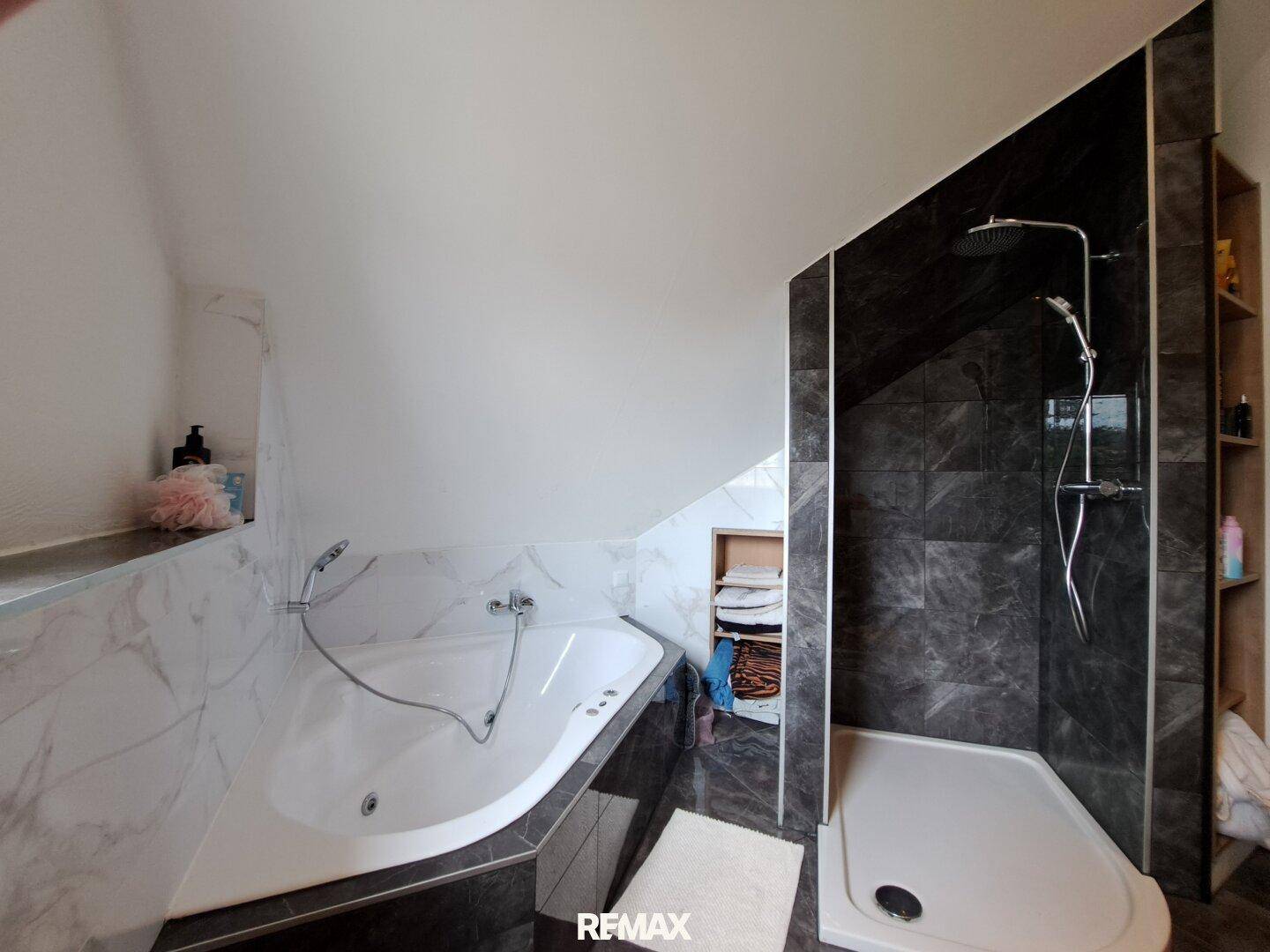 Modernes Badezimmer mit Badewanne, Dusche und dunklen Fliesen unter einer Dachschräge.
