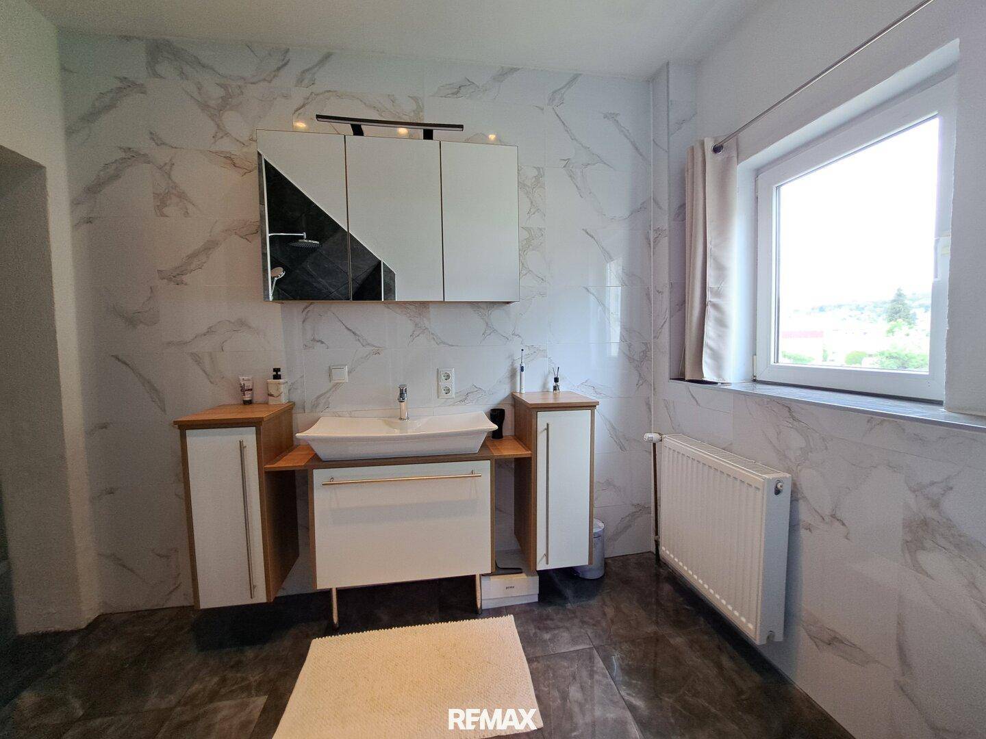 Helles Badezimmer mit modernem Waschtisch, Spiegelschrank und Marmorfliesen.