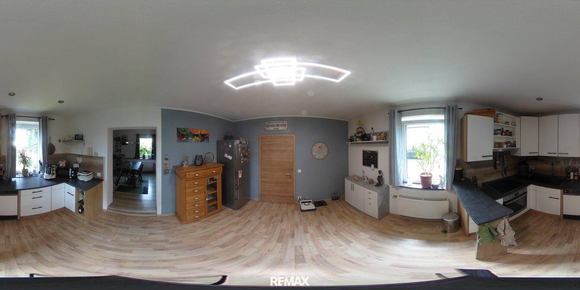 Offene Küche mit weißen Schränken, dunklen Arbeitsplatten und hellem Laminatboden.