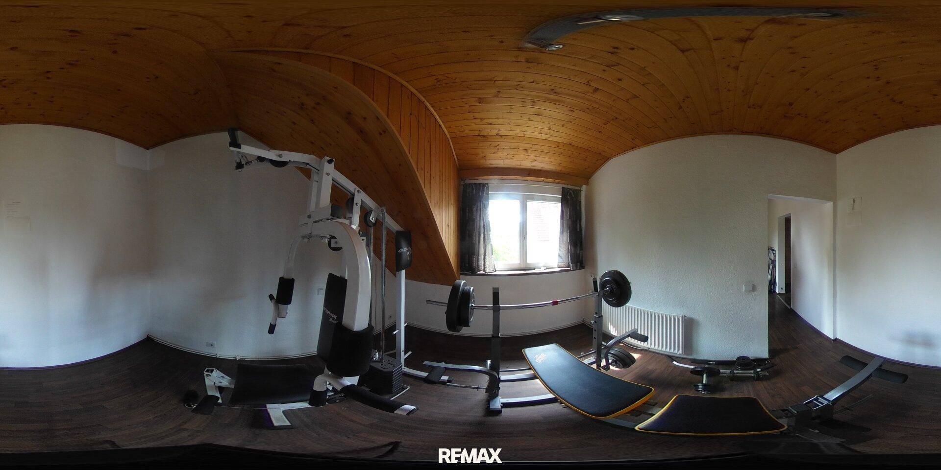 Panoramaansicht eines Fitnessraums mit verschiedenen Trainingsgeräten und Holzdecke.