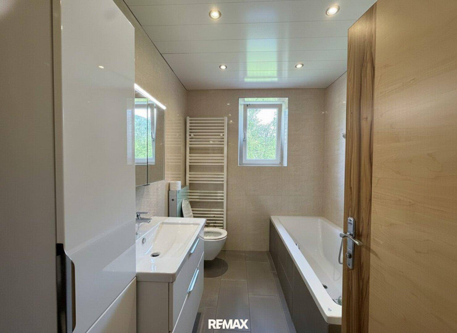 Modernes Badezimmer mit Badewanne, Waschtisch, WC und beheiztem Handtuchhalter.