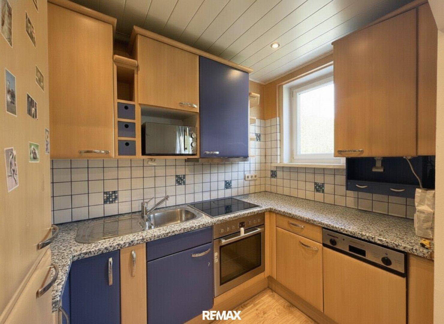 Funktionale Küche mit blauen und holzfarbenen Schränken, Fliesenrückwand und Fenster.