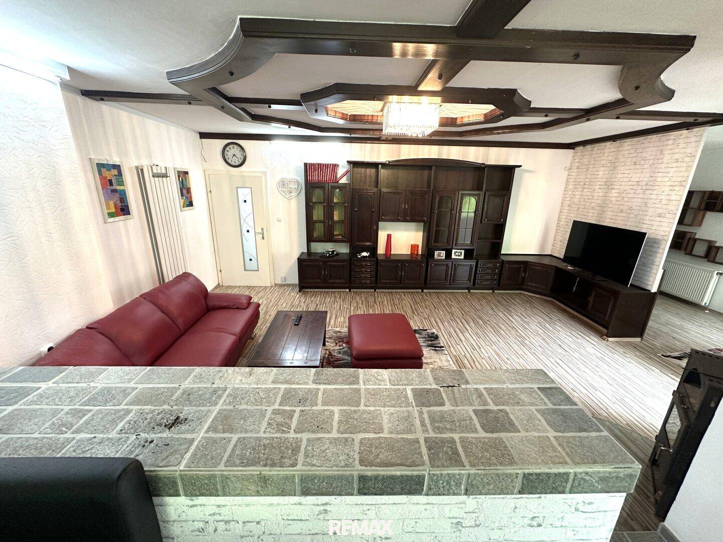 Gemütliches Wohnzimmer mit rotem Sofa, dunklen Holzmöbeln und dekorativer Decke.
