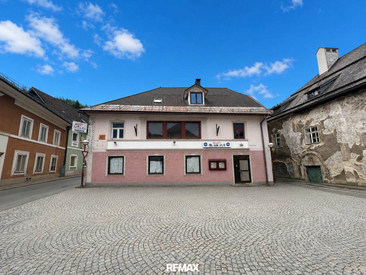 Historisches Gebäude mit rosafarbener Fassade an einem gepflasterten Stadtplatz.