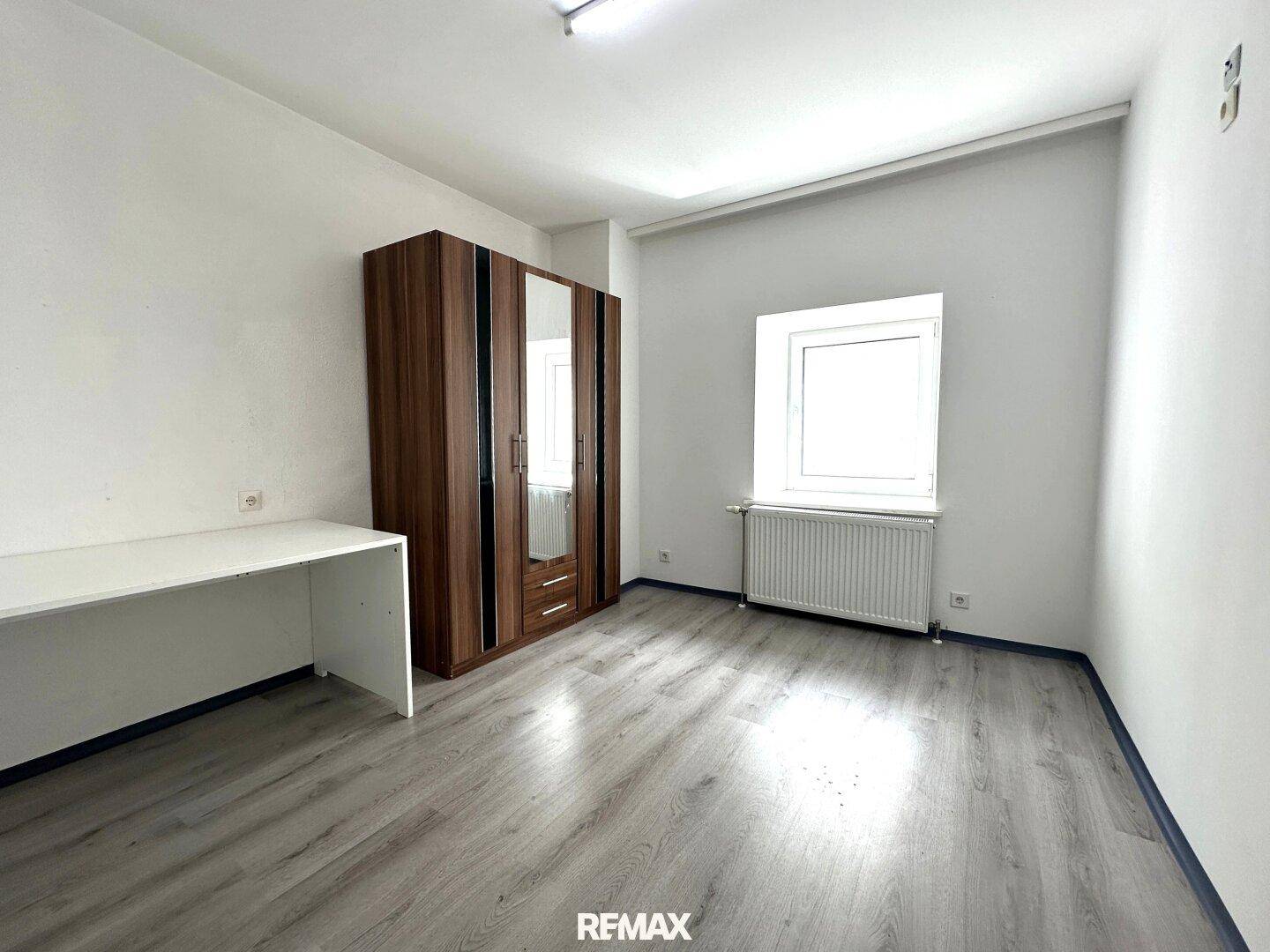Helles Schlafzimmer mit Kleiderschrank, Schreibtisch und modernem Laminatboden.