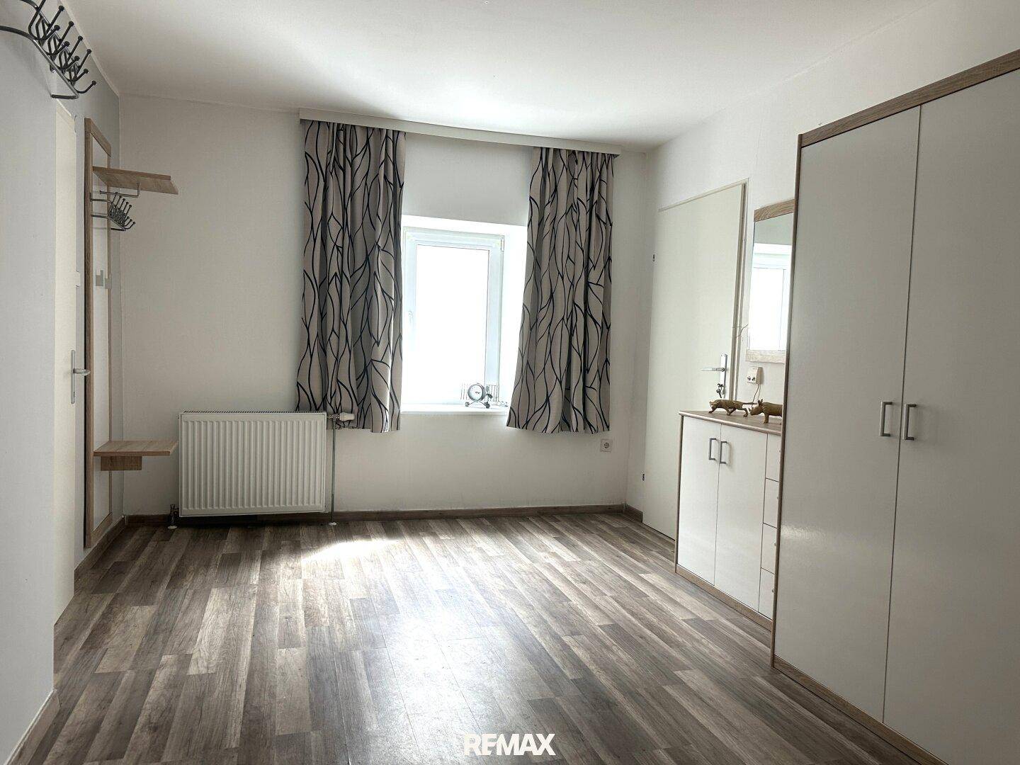 Geräumiges Zimmer mit Laminatboden, Fenster und einem großen Kleiderschrank.
