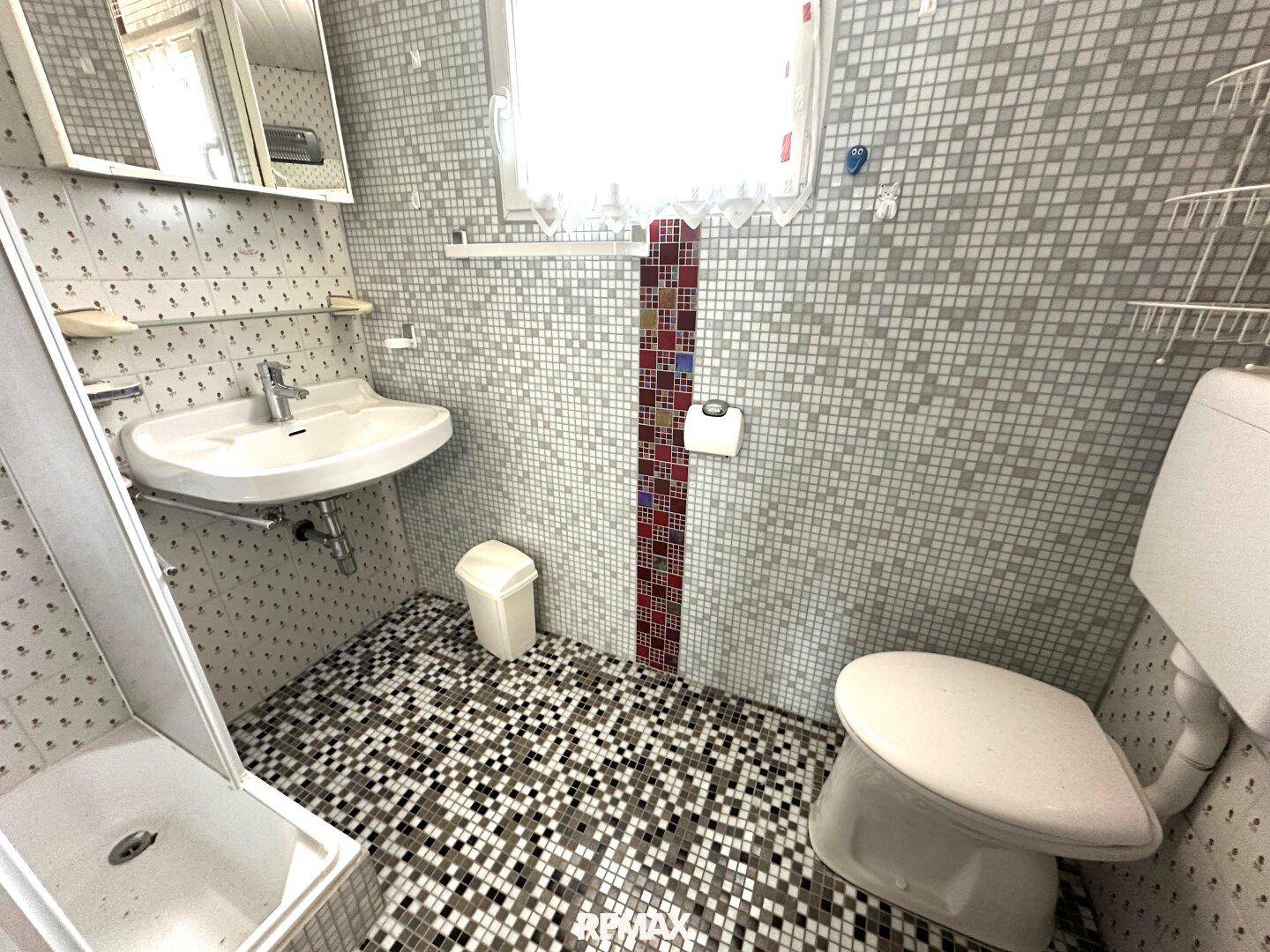 Kleines Badezimmer mit Mosaikfliesen, Dusche, WC und Fenster für Tageslicht.