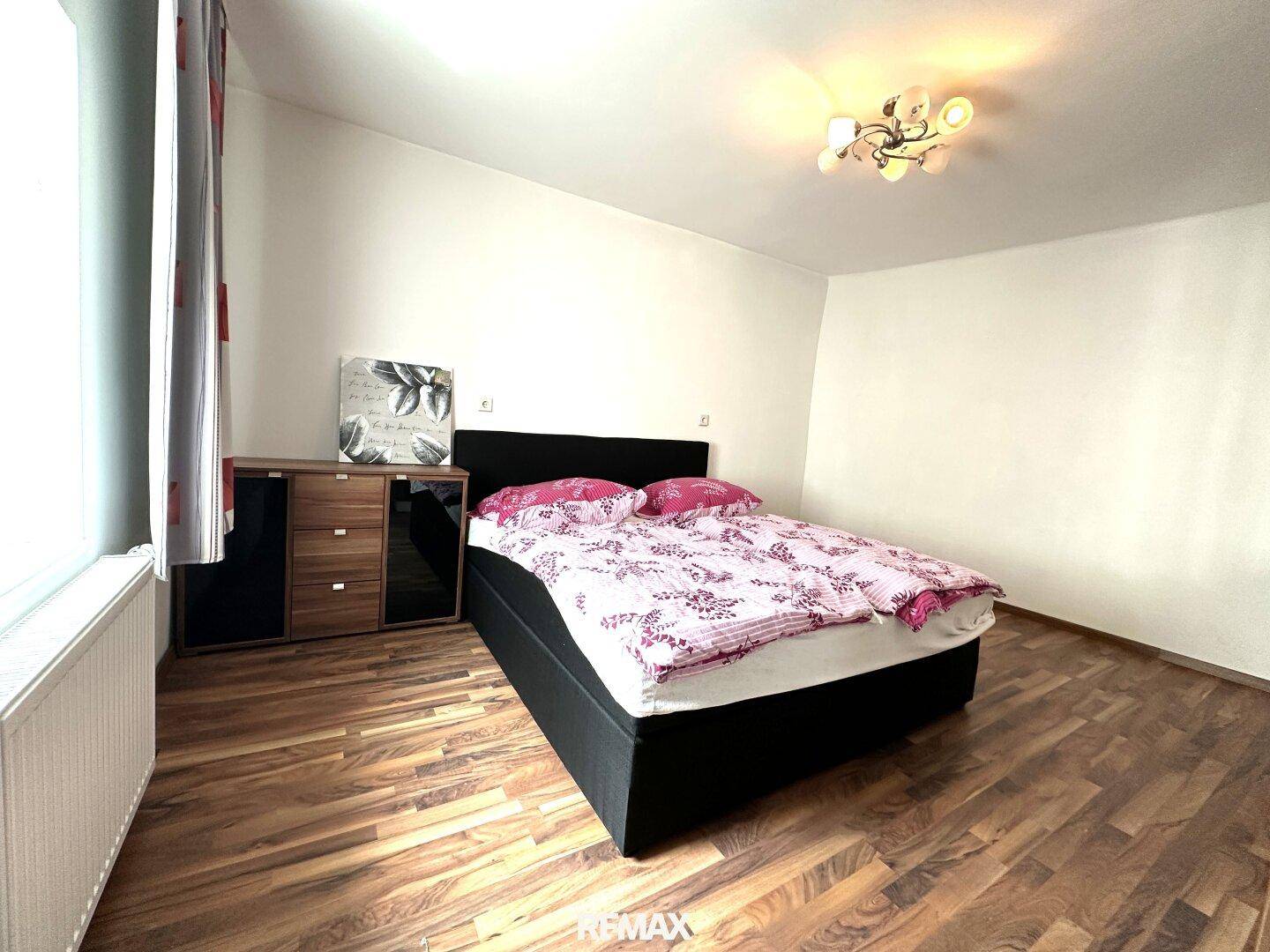 Schlafzimmer mit Doppelbett, Holzoptik-Boden und schlichter Einrichtung.
