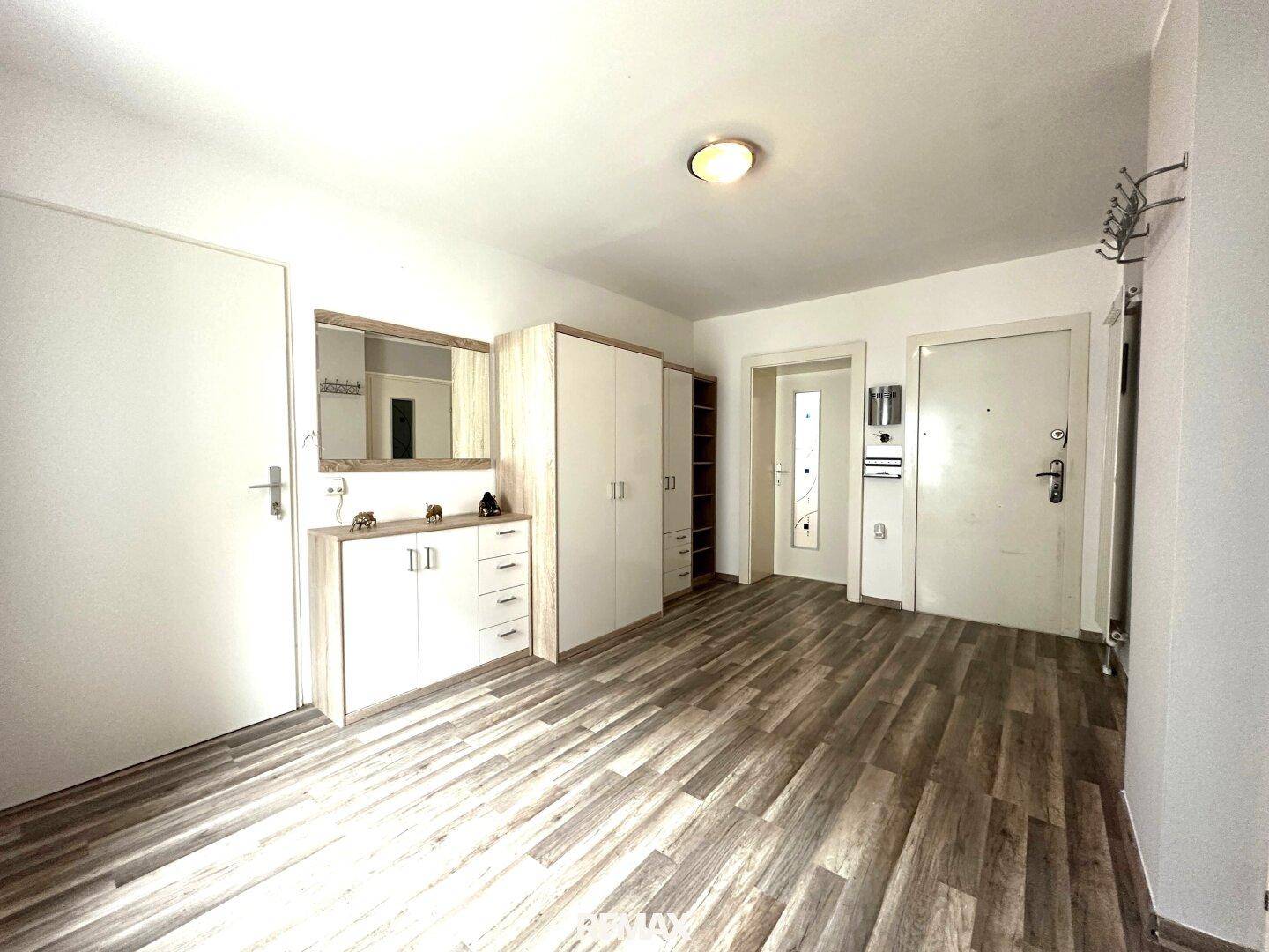 Heller Flur mit Holzoptik-Boden, Garderobe und Zugang zu weiteren Räumen.