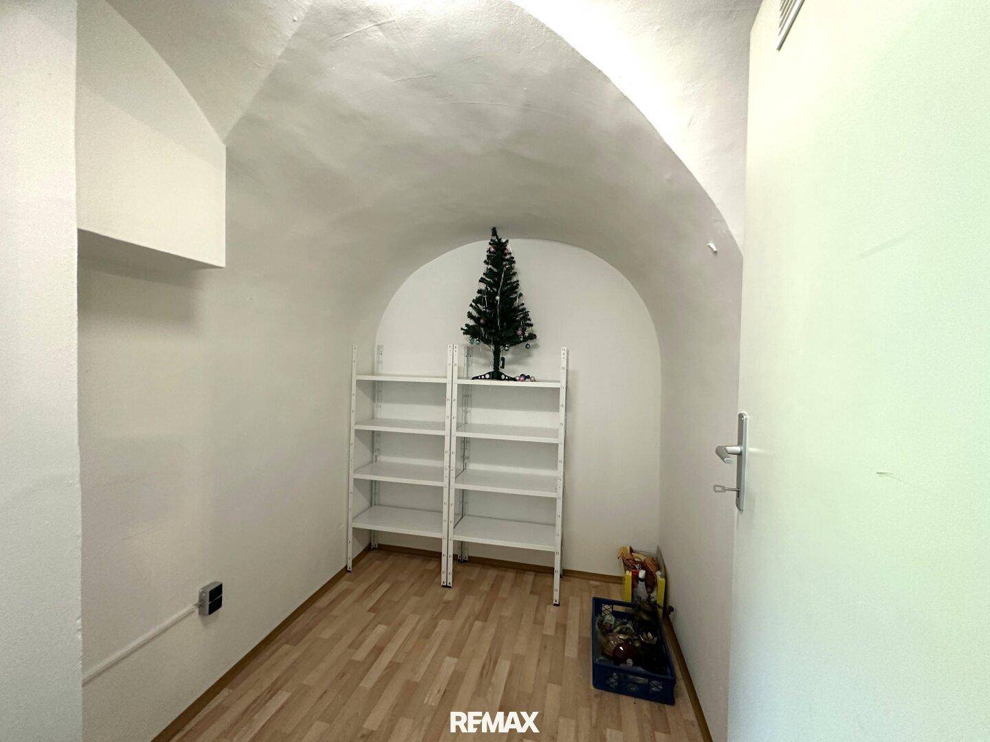 Lagerraum oder Keller mit Gewölbedecke, Regalen und Laminatboden.