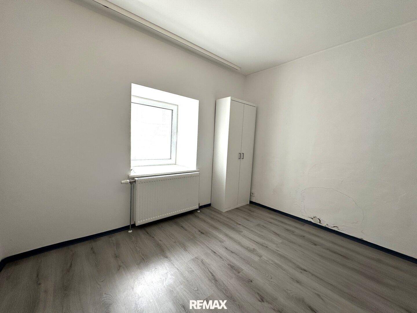 Unmöbliertes Zimmer mit Laminatboden, Fenster und einem einfachen Kleiderschrank.