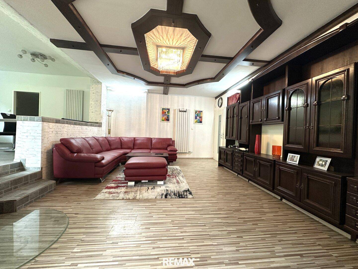 Geräumiges Wohnzimmer mit rotem Sofa, dunklen Holzmöbeln und dekorativer Decke.