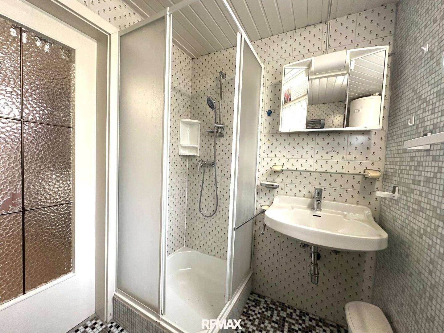 Kleines Badezimmer mit Duschkabine, Waschbecken und gemusterten Fliesen.
