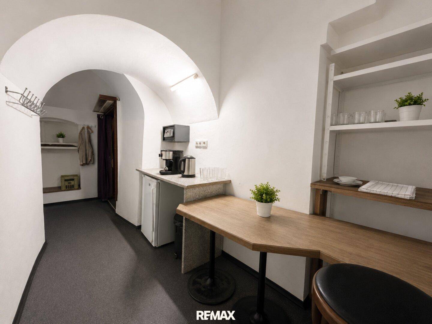 Kleiner Küchenbereich mit Gewölbedecke, Spüle, Kühlschrank und Arbeitsplatte.