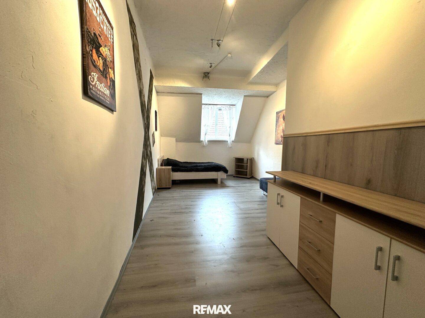 Zimmer im Dachgeschoss mit schrägen Decken, Laminatboden und einfacher Einrichtung.