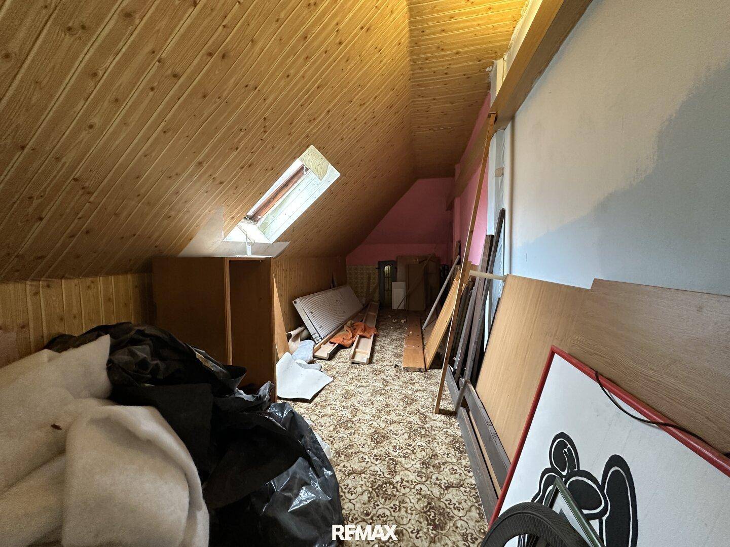 Dachboden mit Holzverkleidung, Dachfenster und gelagerten Gegenständen.