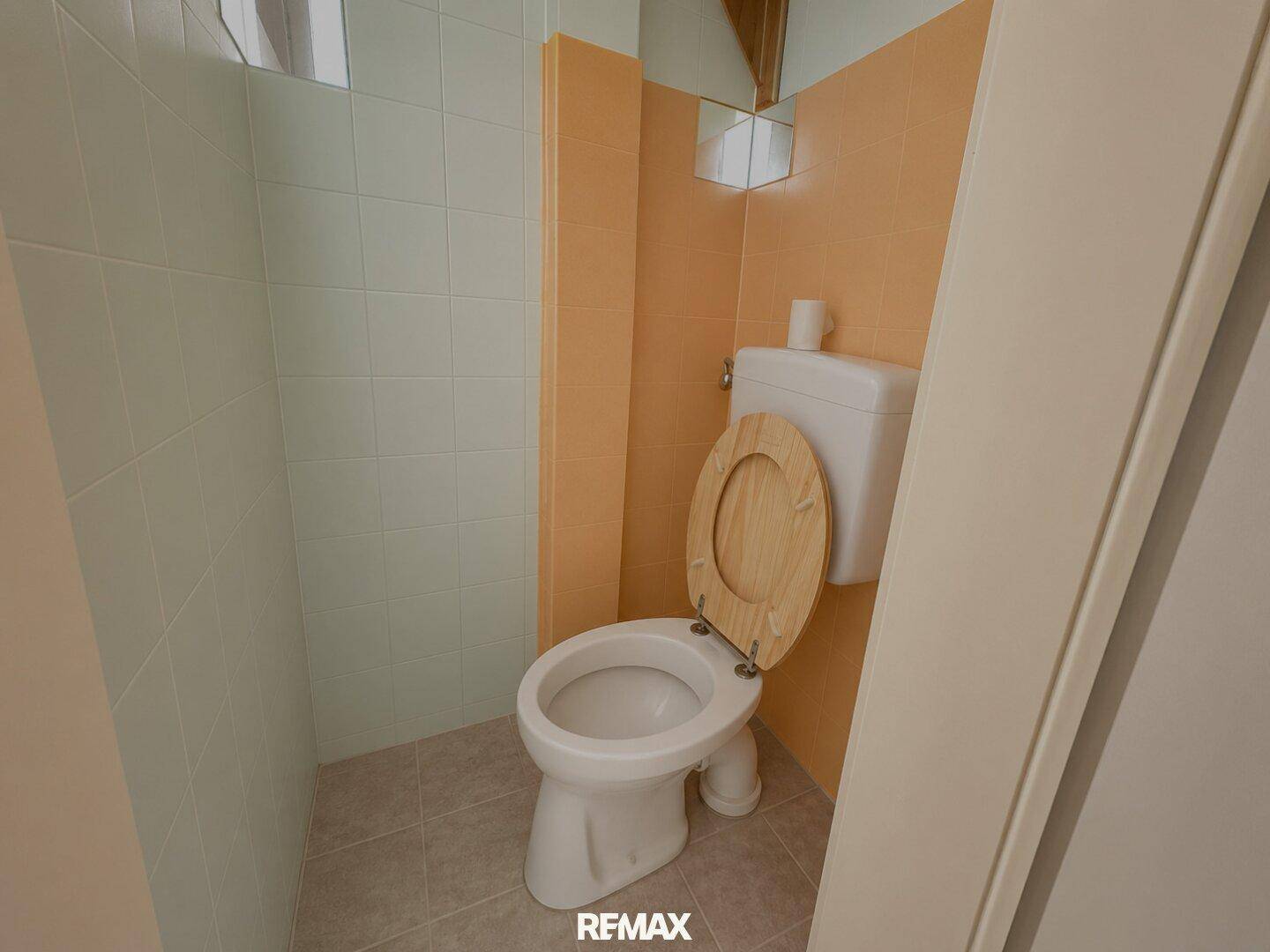 Kleines WC mit Toilette und gefliesten Wänden.