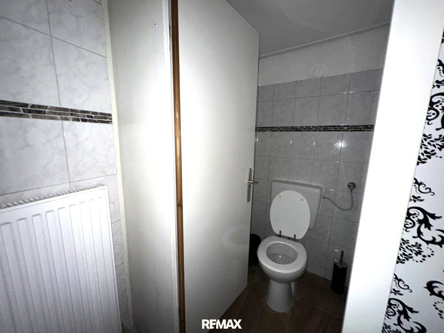 Separate Toilette mit weißem WC, Heizkörper und gefliesten Wänden.