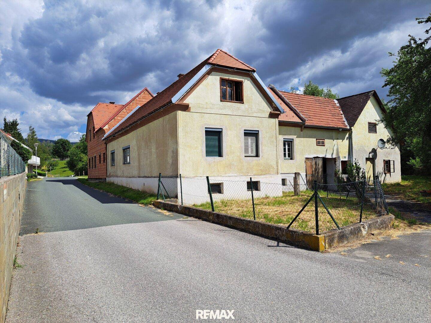Altes Wohnhaus mit gelber Fassade und rotem Ziegeldach unter bewölktem Himmel.