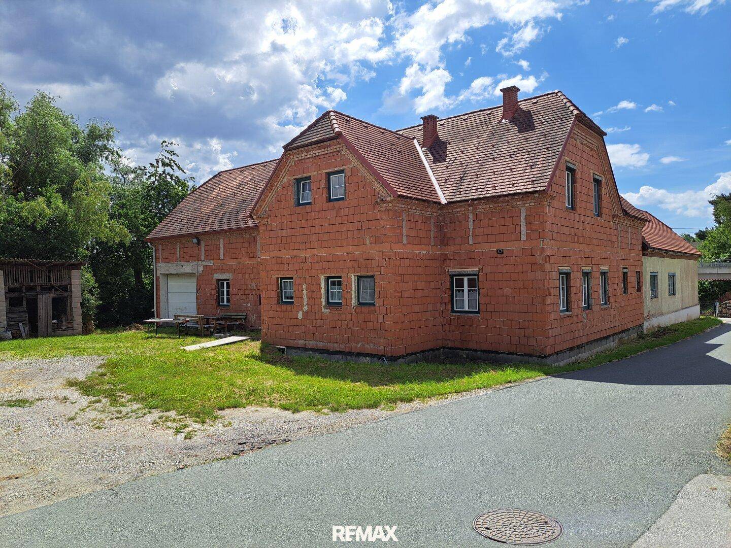 Backsteinhaus mit rotem Ziegeldach und angrenzendem Nebengebäude in ländlicher Umgebung.