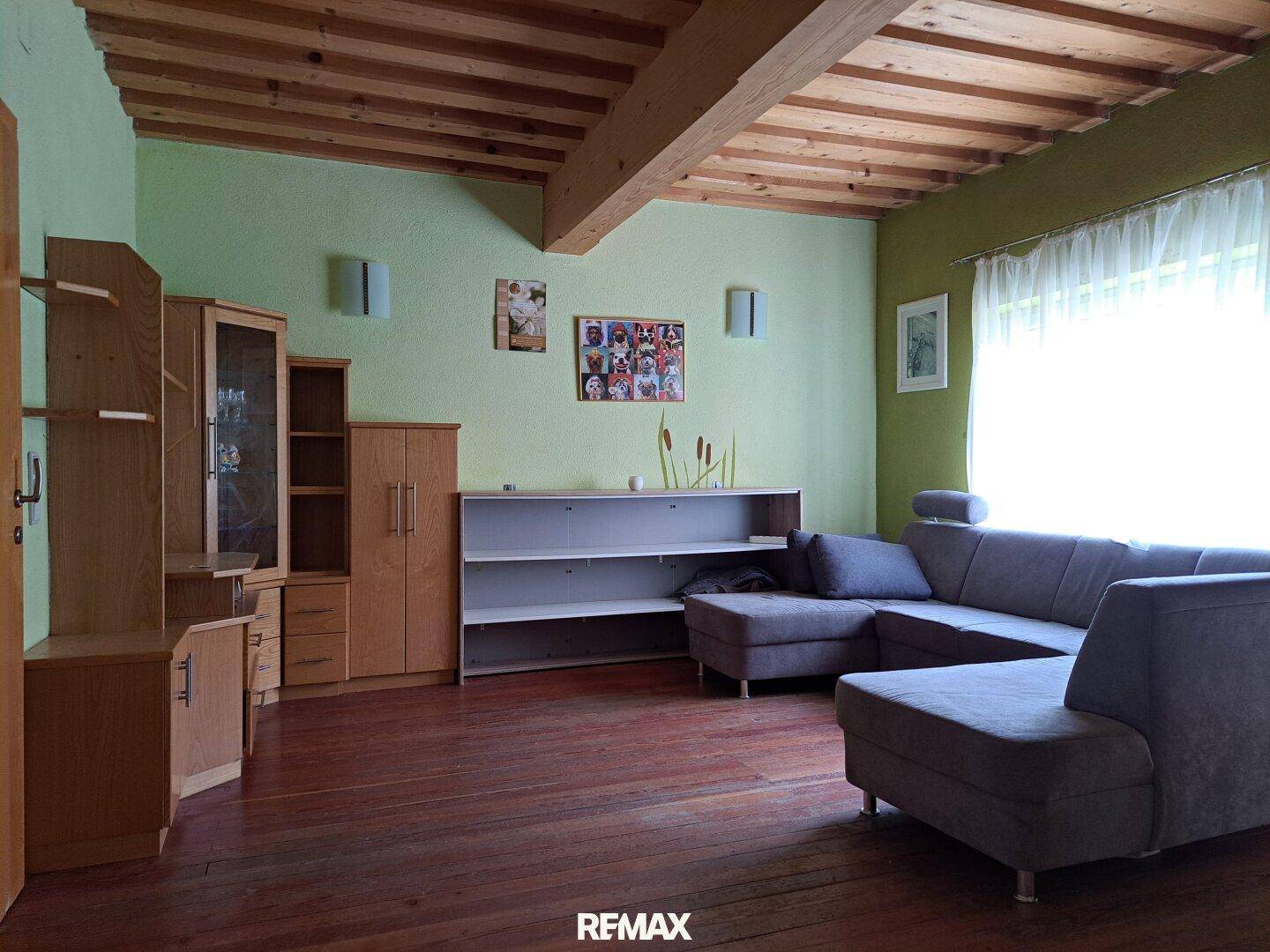 Gemütliches Wohnzimmer mit Holzbalkendecke, grün gestrichenen Wänden und Sofa.