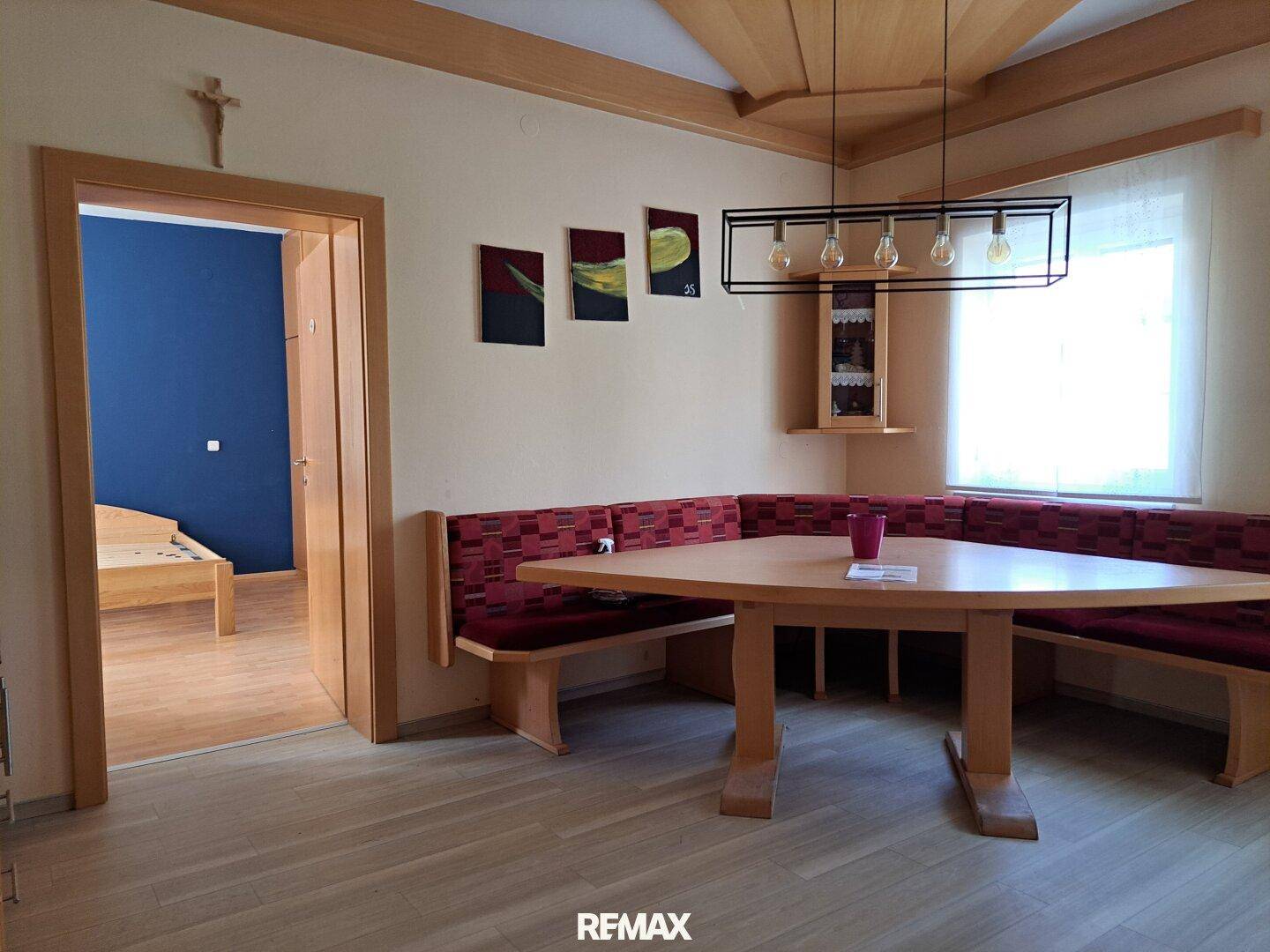 Essbereich mit Holzbänken, Esstisch und Blick in ein angrenzendes Schlafzimmer.