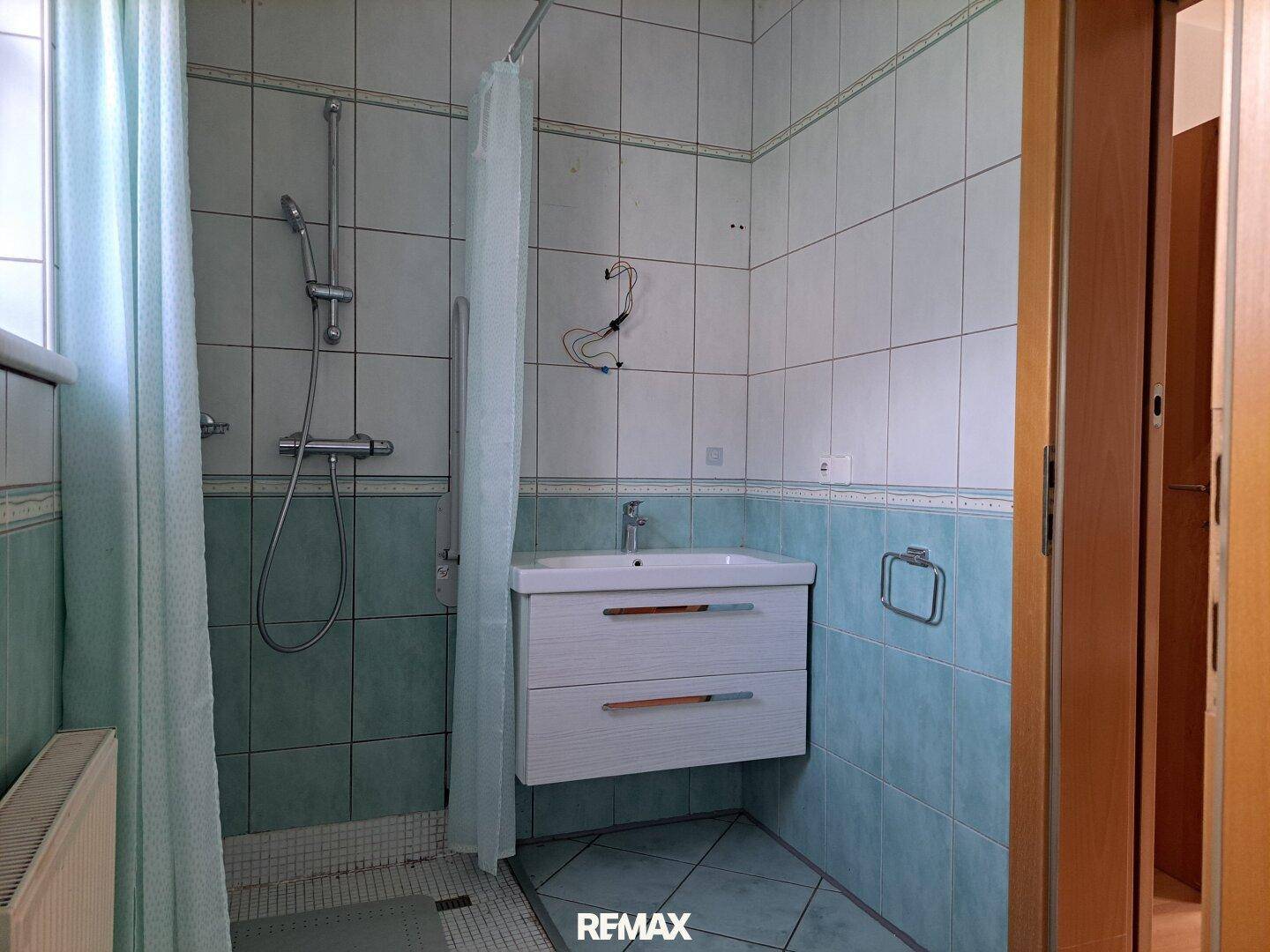 Badezimmer mit hellblauen Fliesen, Duschbereich und modernem Waschtisch.