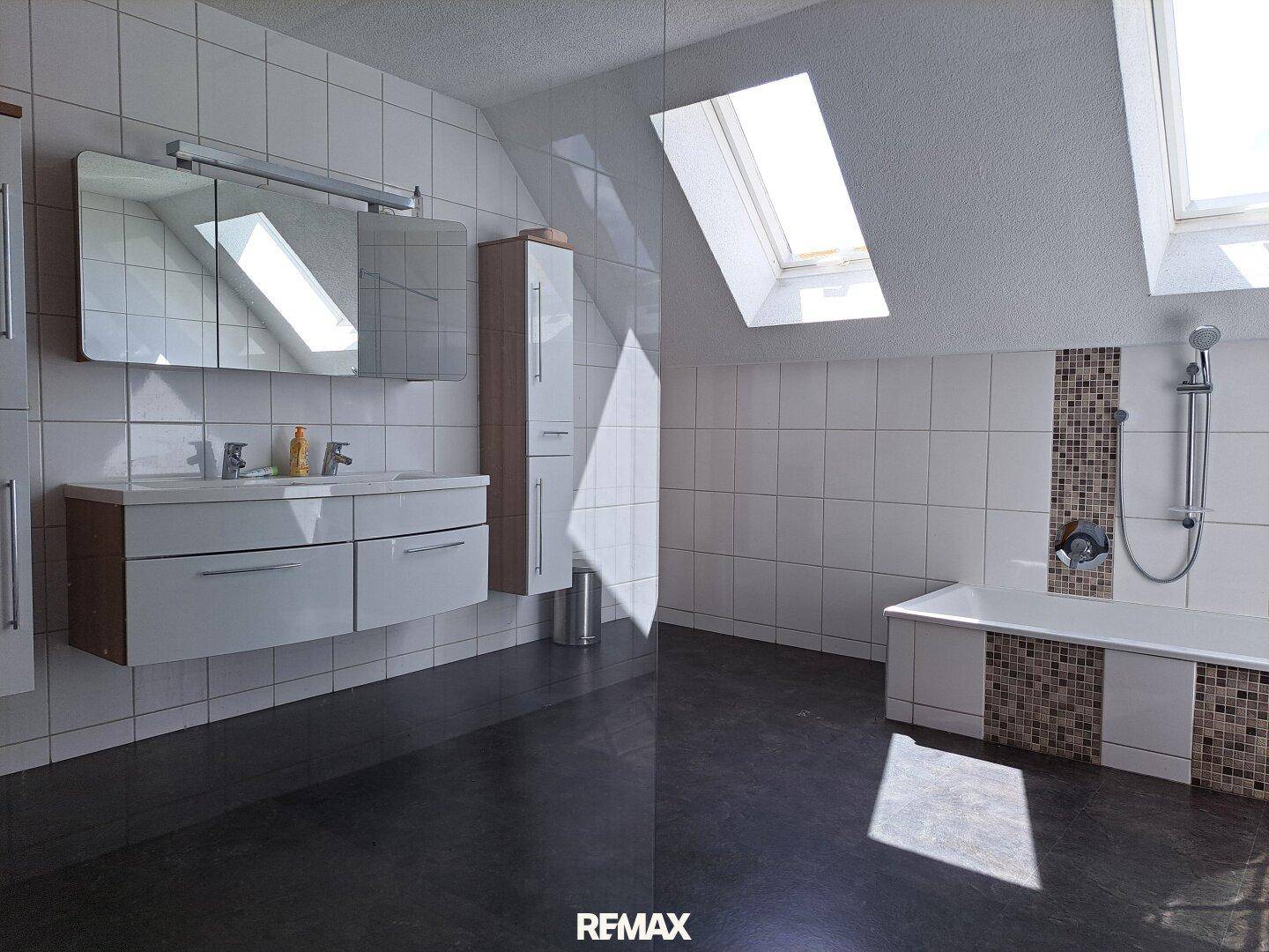 Helles Badezimmer mit Dachfenstern, Doppelwaschbecken und Badewanne mit Duschfunktion.