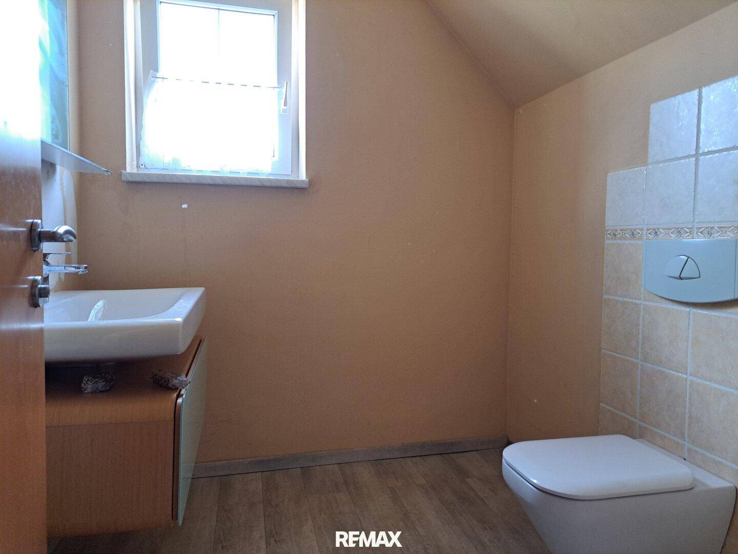Kleines Badezimmer mit Waschbecken, Toilette und Fenster im Dachgeschoss.