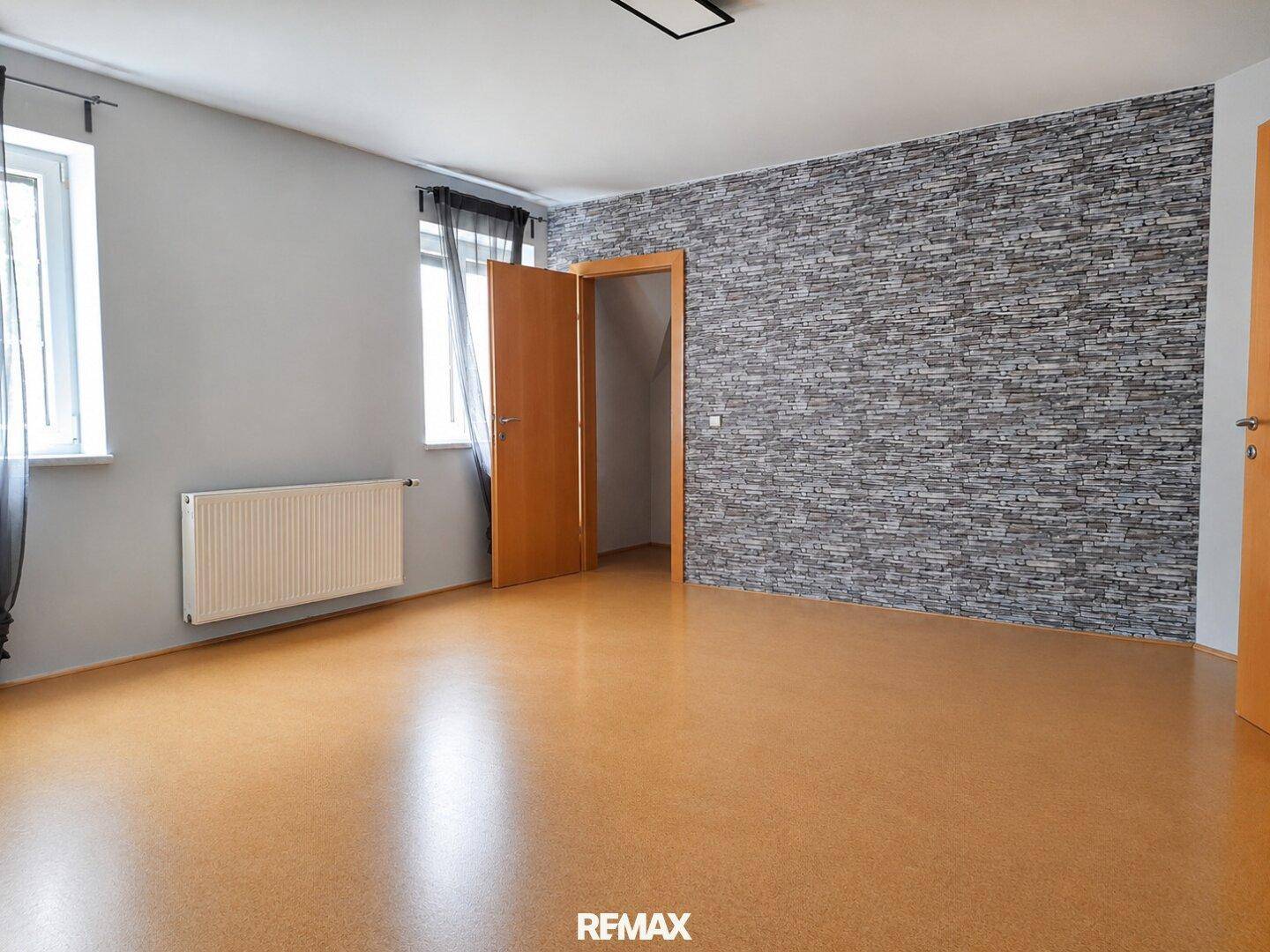 Geräumiges Zimmer mit Korkboden und einer Akzentwand in Steinoptik.
