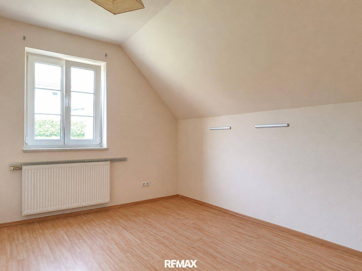 Helles Schlafzimmer im Dachgeschoss mit schrägen Wänden und Fenster.