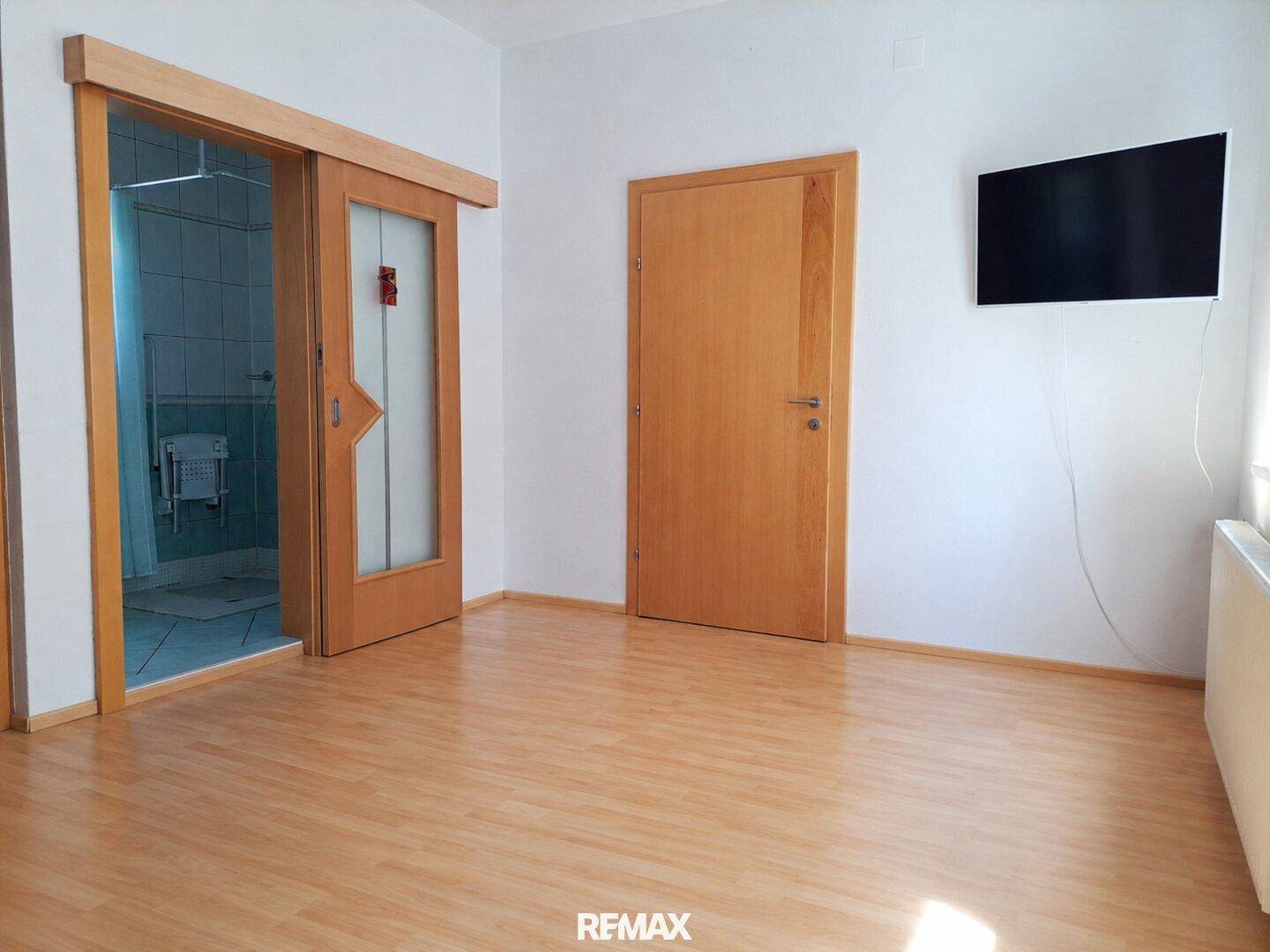 Schlafzimmer mit Laminatboden, Schiebetür zum Bad und Wandfernseher.
