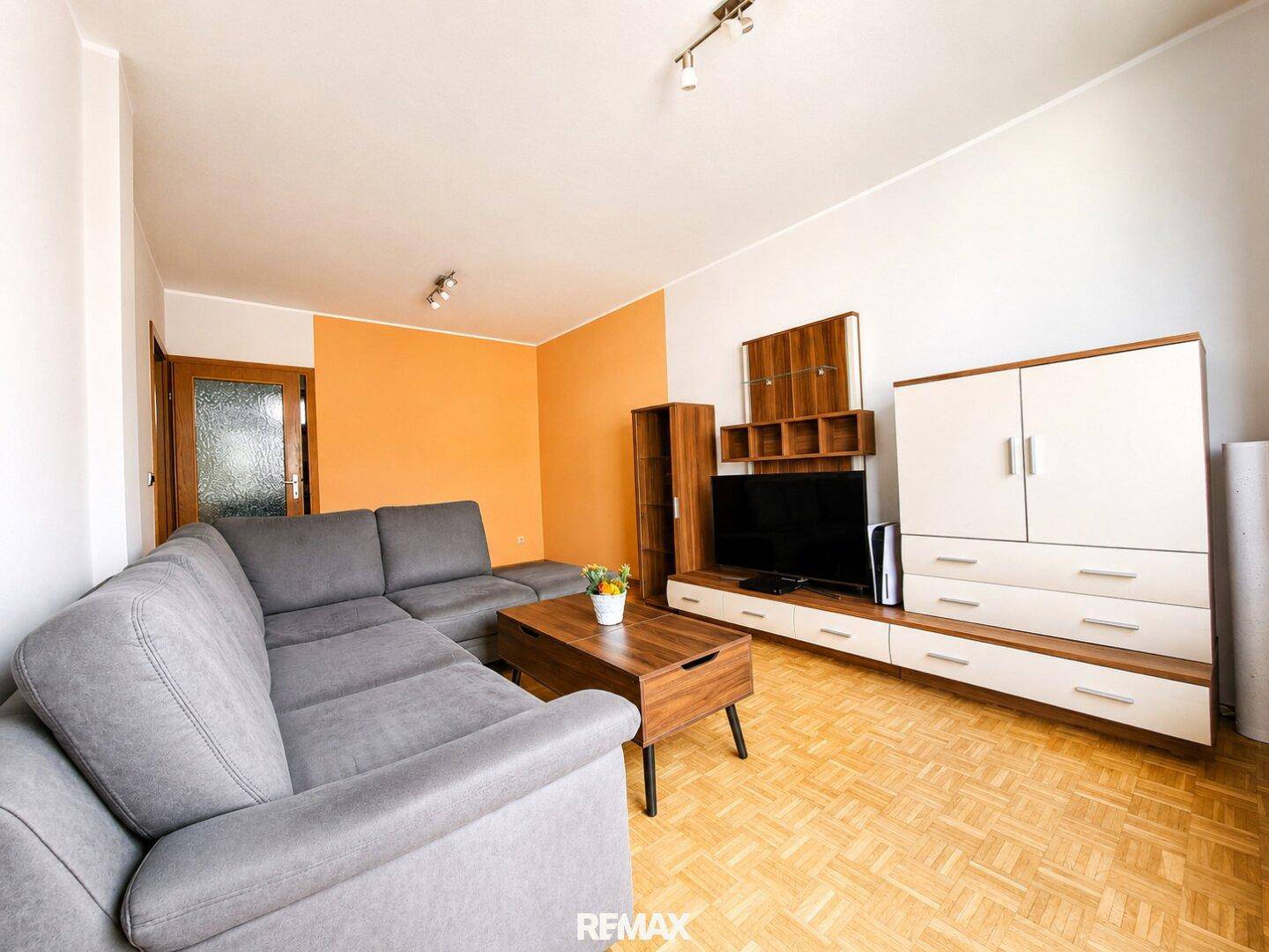 Helles Wohnzimmer mit Parkettboden, bequemer Couch und moderner TV-Wand mit Stauraum.