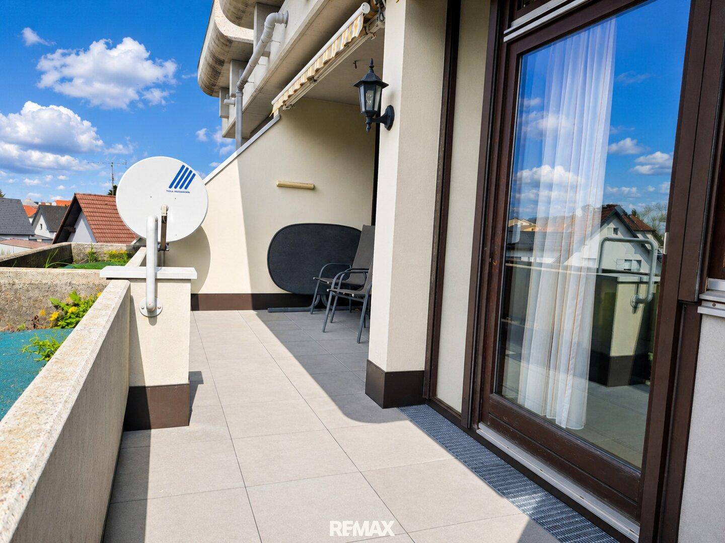 Heller Balkon mit Fliesenboden und Blick auf die umliegenden Häuser unter blauem Himmel.