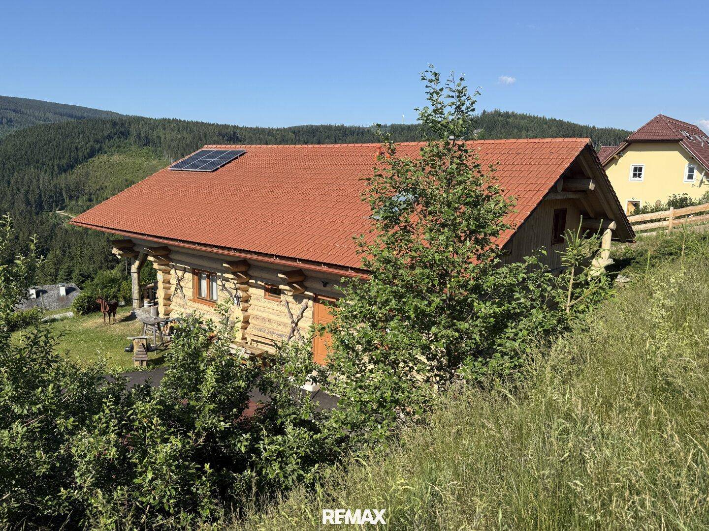 Blockhaus mit rotem Ziegeldach und Photovoltaikanlage, eingebettet in die Berglandschaft.