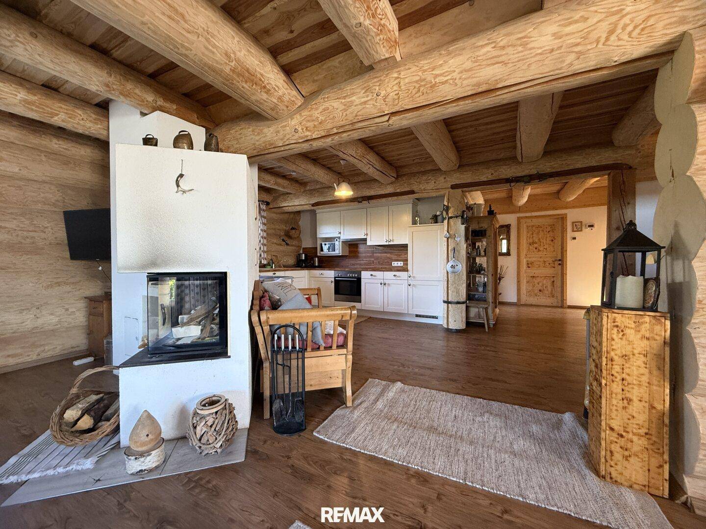 Heller Wohnbereich mit Kamin und offener Küche, charakterisiert durch Holzbalken und rustikalen Charme.
