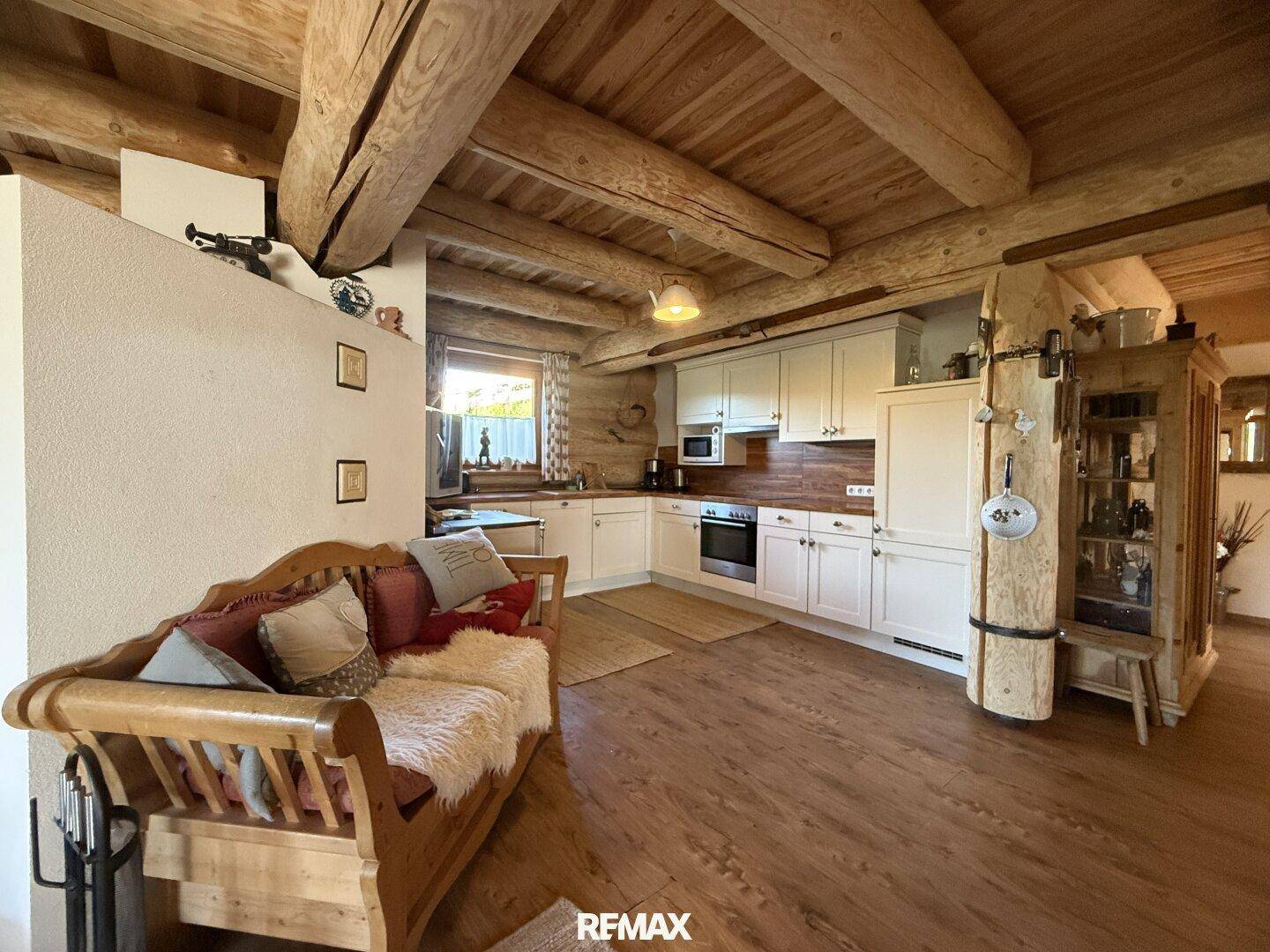 Gemütlicher offener Wohnbereich mit Holzbalkendecke und integrierter Küche im Landhausstil.