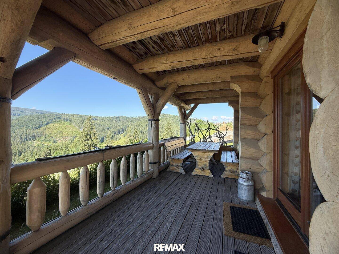 Überdachter Balkon mit rustikalen Holzmöbeln und weitem Blick auf die bewaldete Landschaft.