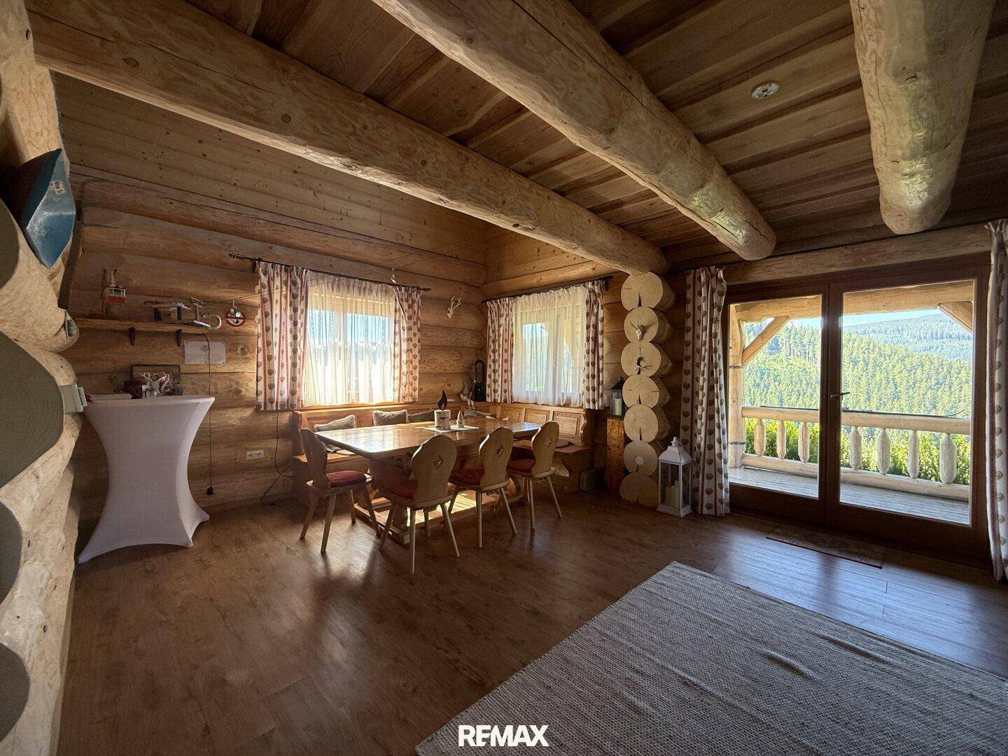 Rustikaler Essbereich mit Holztisch und Stühlen, Holzbalkendecke und Zugang zum Balkon.