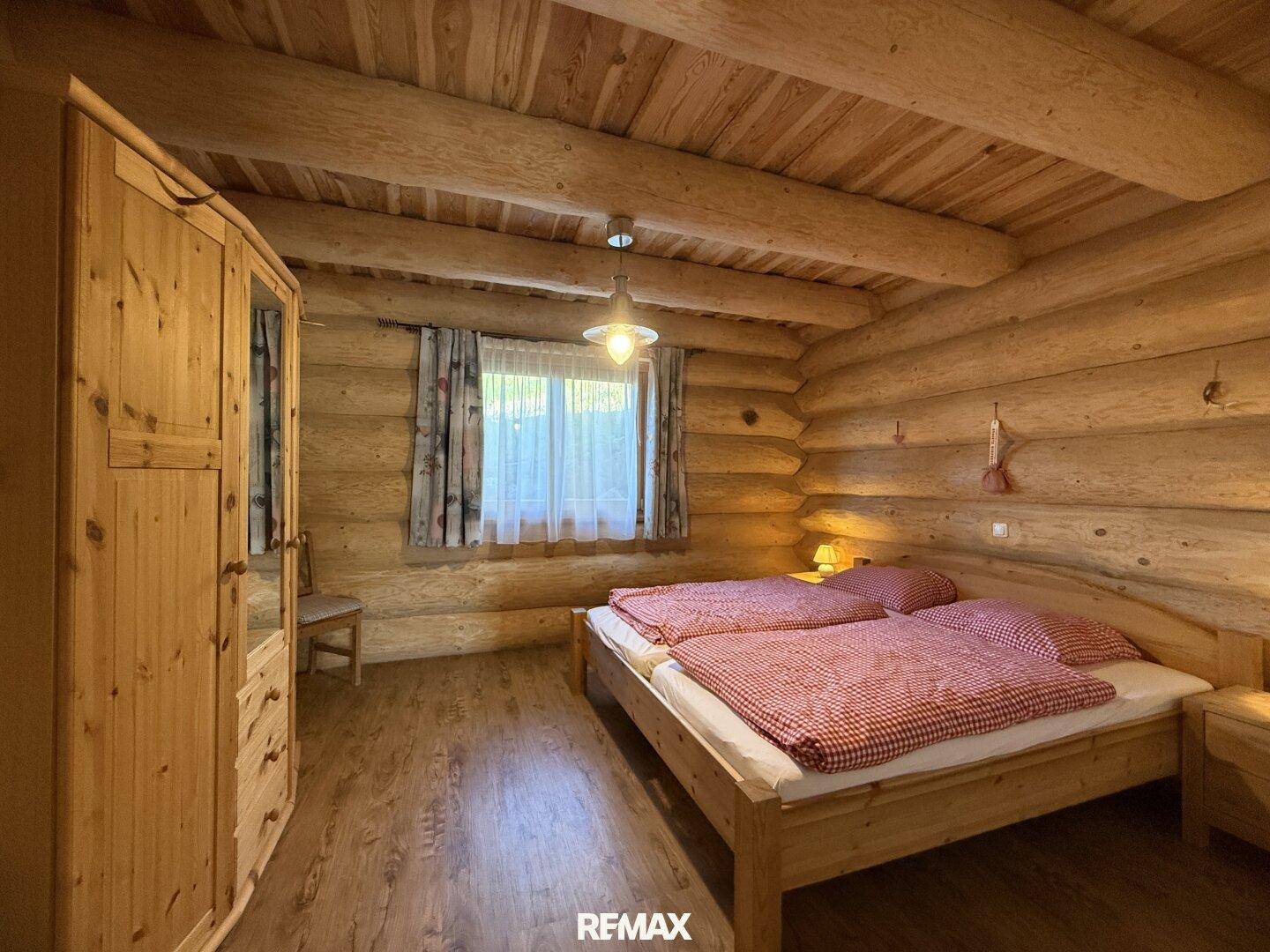 Gemütliches Schlafzimmer mit Doppelbett, Holzmöbeln und Holzbalkendecke im Landhausstil.