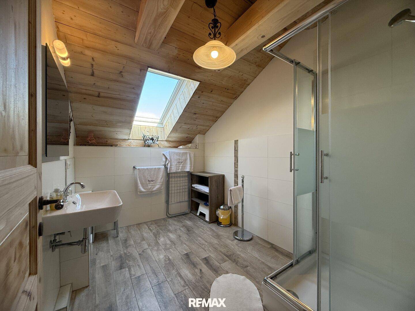 Modernes Badezimmer im Dachgeschoss mit Duschkabine, Waschbecken und Dachfenster.