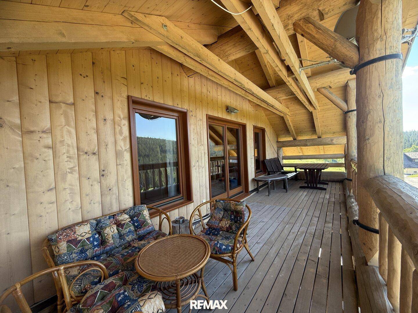 Überdachter Balkon mit gemütlichen Sitzmöbeln und Blick auf die grüne Umgebung.