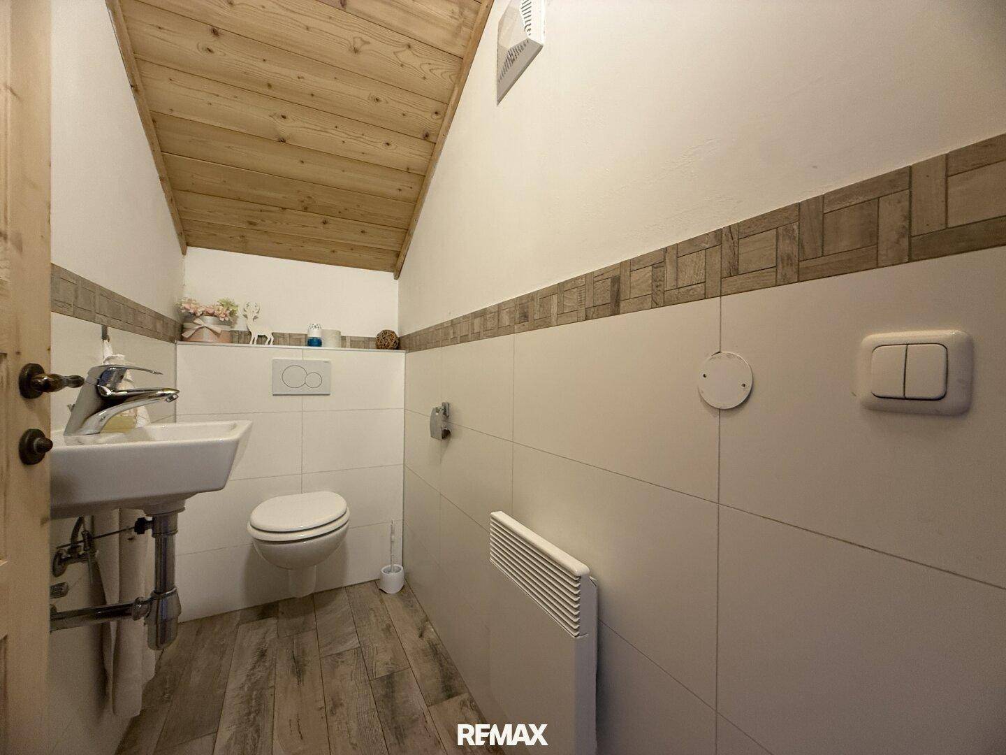 Kleines Gäste-WC mit Waschbecken, Toilette und Holzdecke im Dachgeschoss.