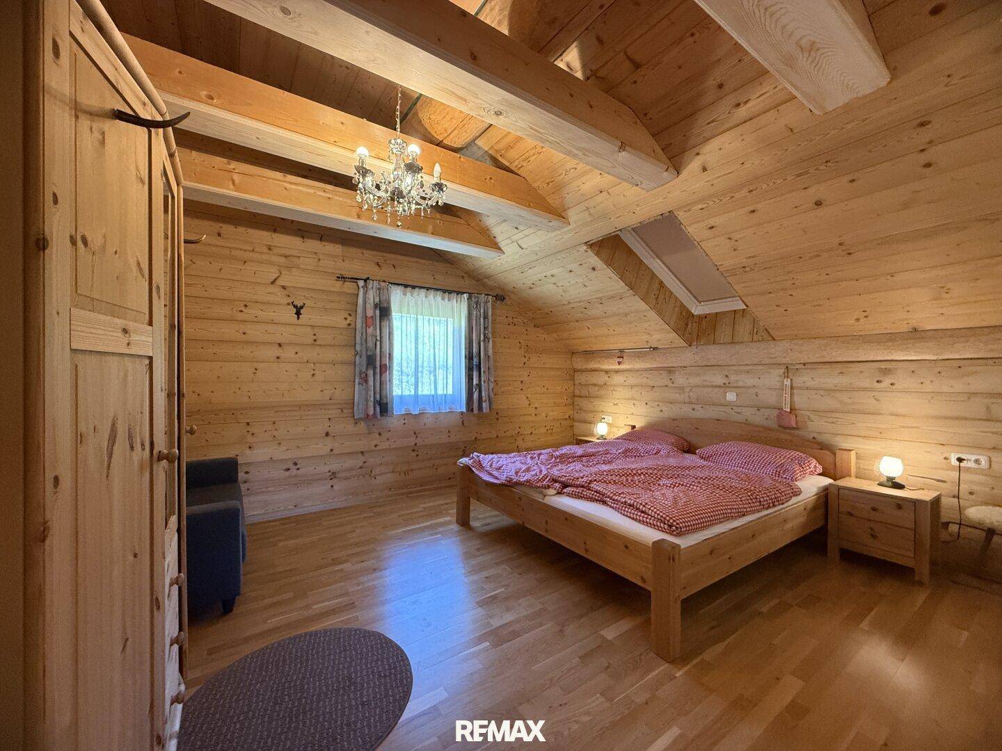 Helles Schlafzimmer im Dachgeschoss mit Doppelbett, Holzvertäfelung und Kronleuchter.